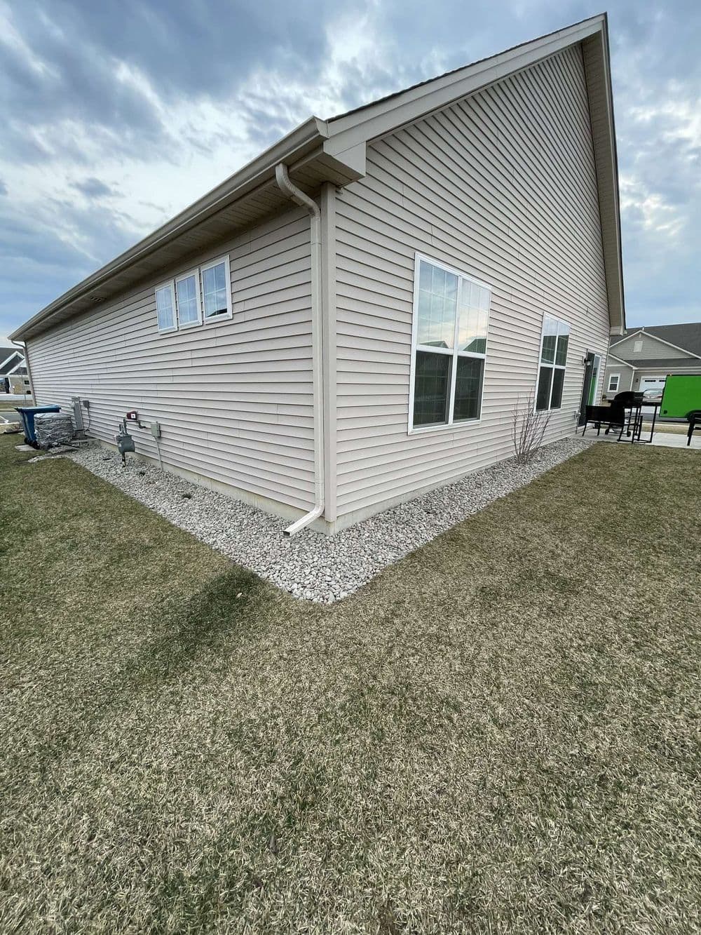 House exterior with light siding, gravel landscaping, and cloudy sky in the background.