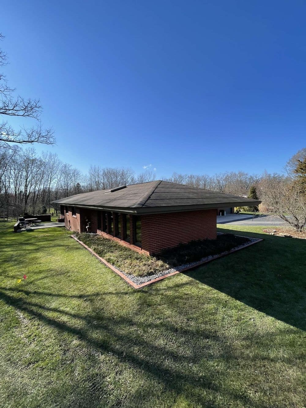 Modern red brick house with a flat roof surrounded by green grass and bare trees under a blue sky.