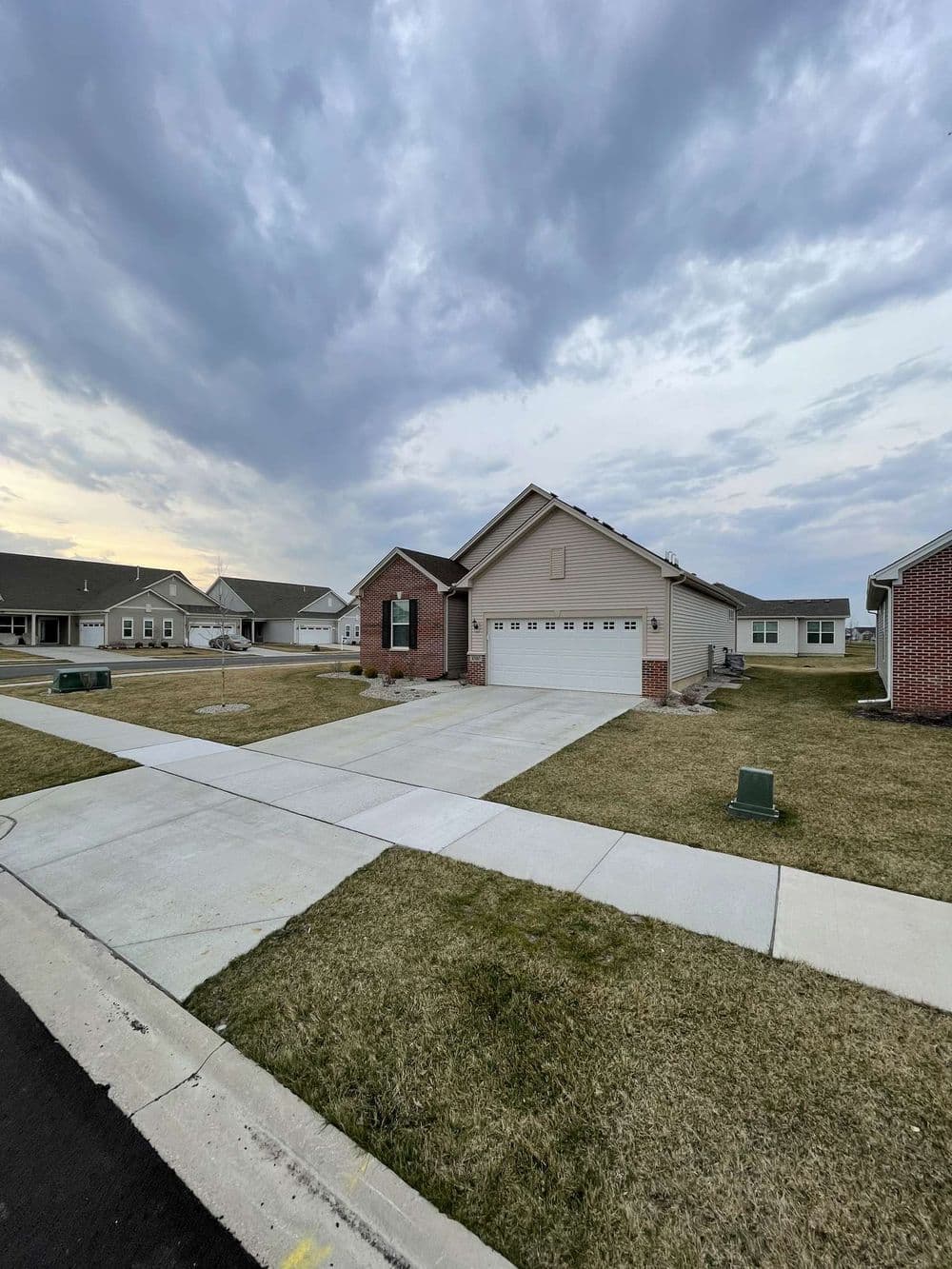 Suburban home with garage on quiet street under cloudy sky, showcasing landscaped yard.
