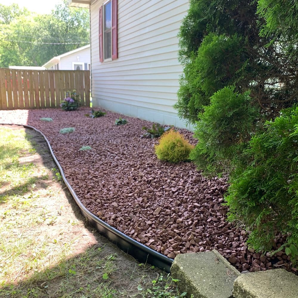 Landscaped garden with decorative stones and low shrubs beside a house, featuring a wooden fence.