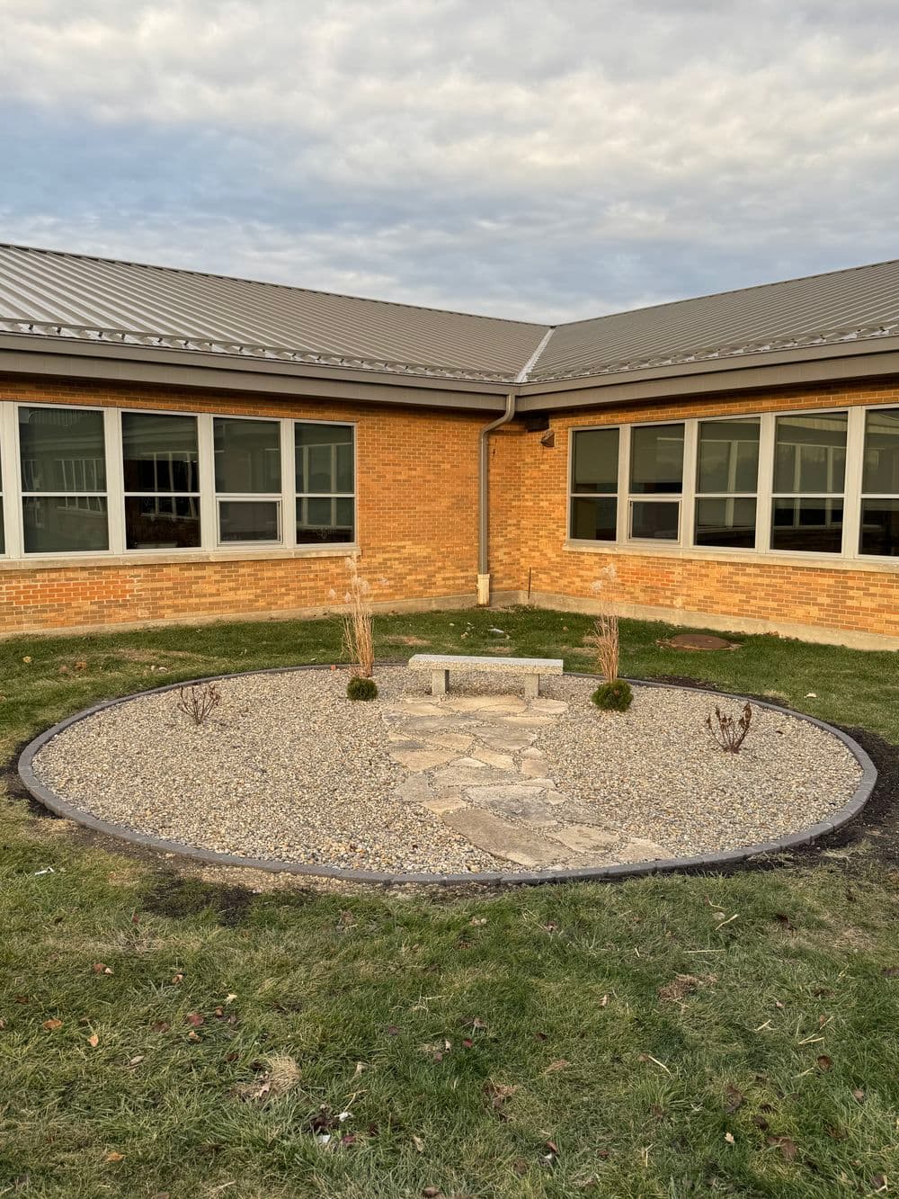 Courtyard garden with stone path and decorative plants, surrounded by brick building windows.