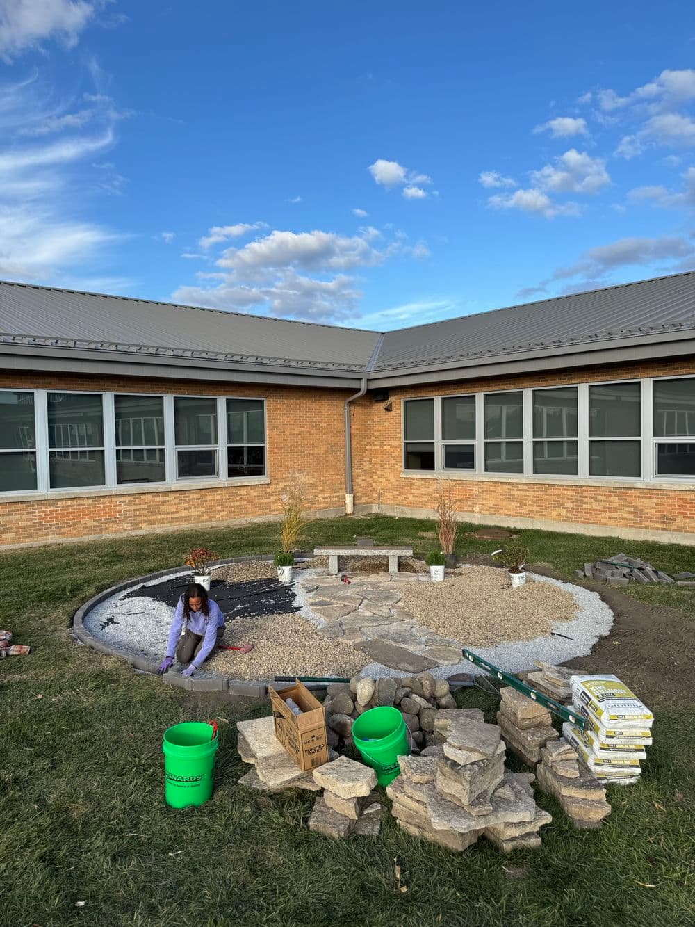 Student landscaping garden with stones, gravel, and plants at school courtyard.