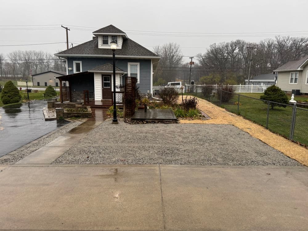 View of a gray house on a rainy day with a landscaped garden and paved walkway.
