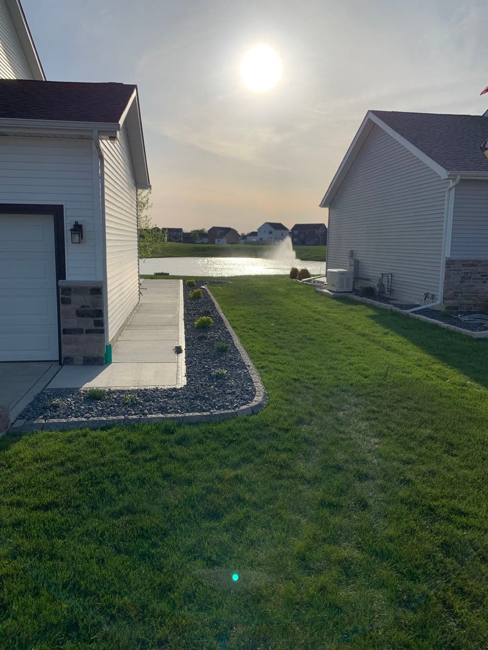 Lakeside view from home showcasing green lawn and sunset reflections on water.
