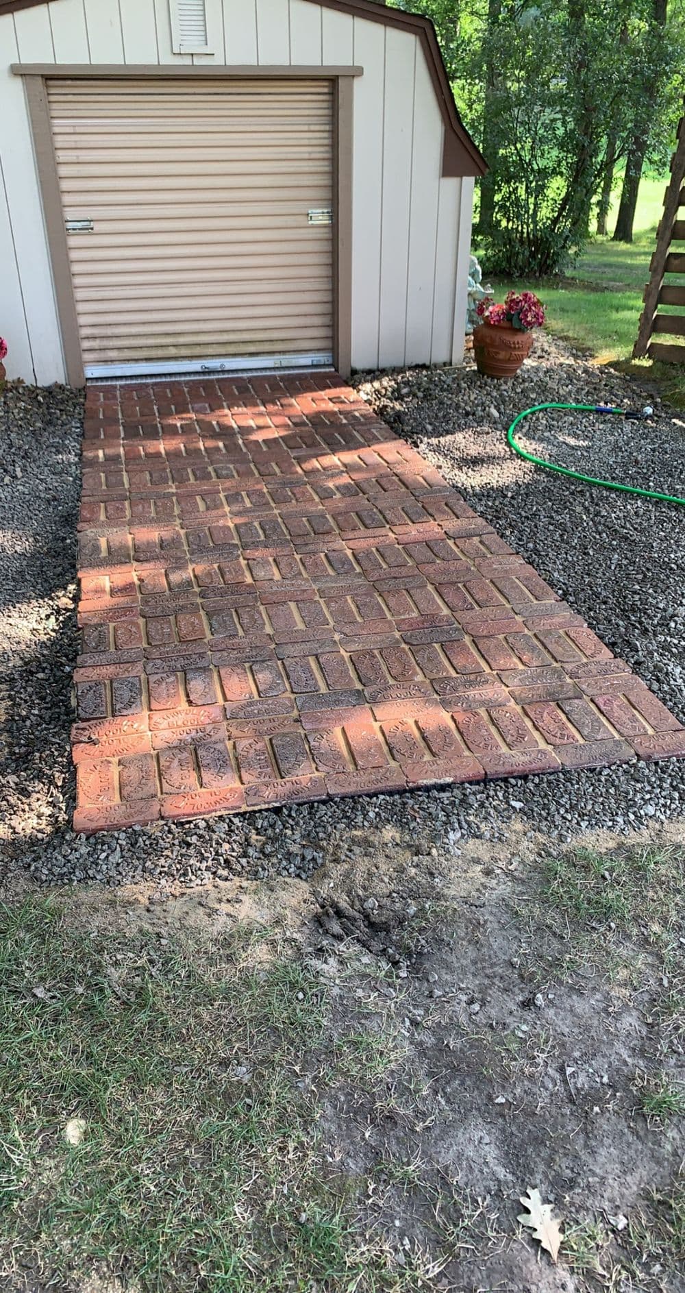 Paved walkway made of red bricks leading to a garden shed in a green landscape.