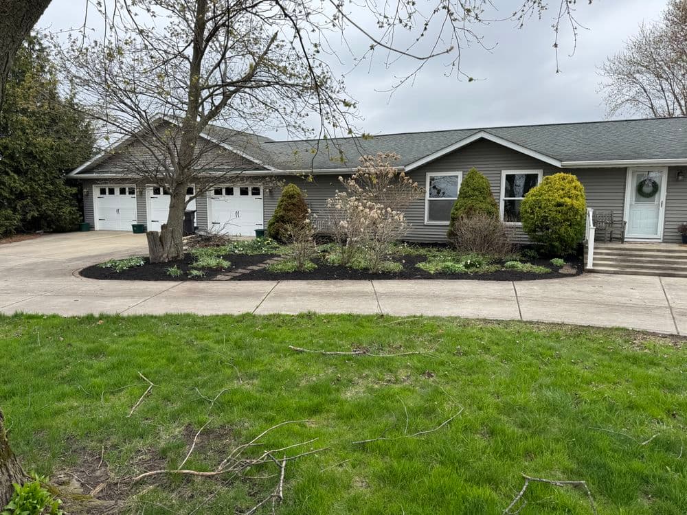 Single-story house with gray siding, green landscaping, and a two-car garage on a cloudy day.