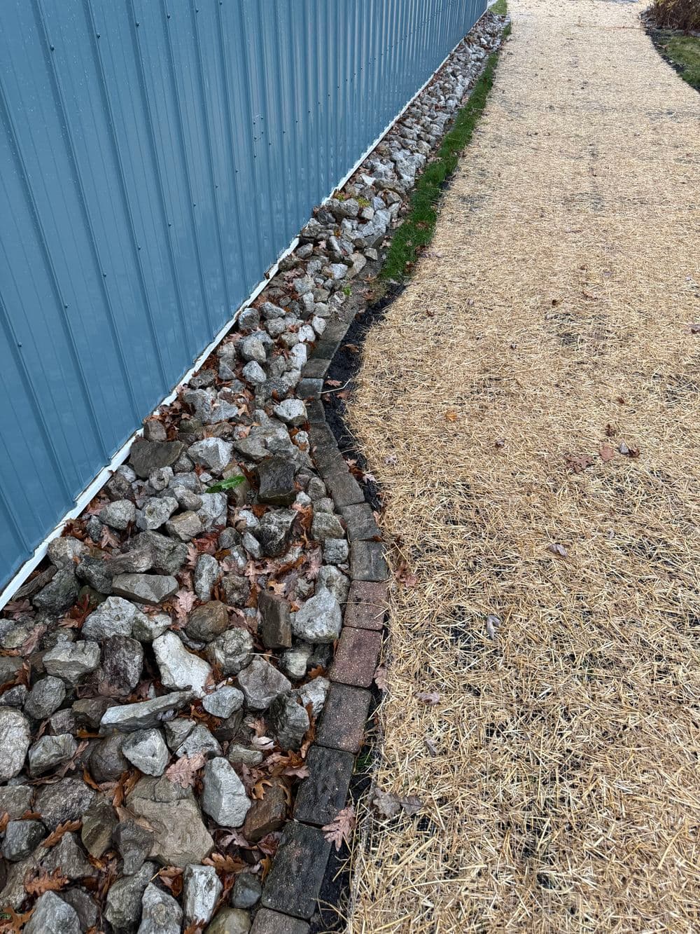 Gravel border along blue building with adjoining straw path in outdoor landscape.