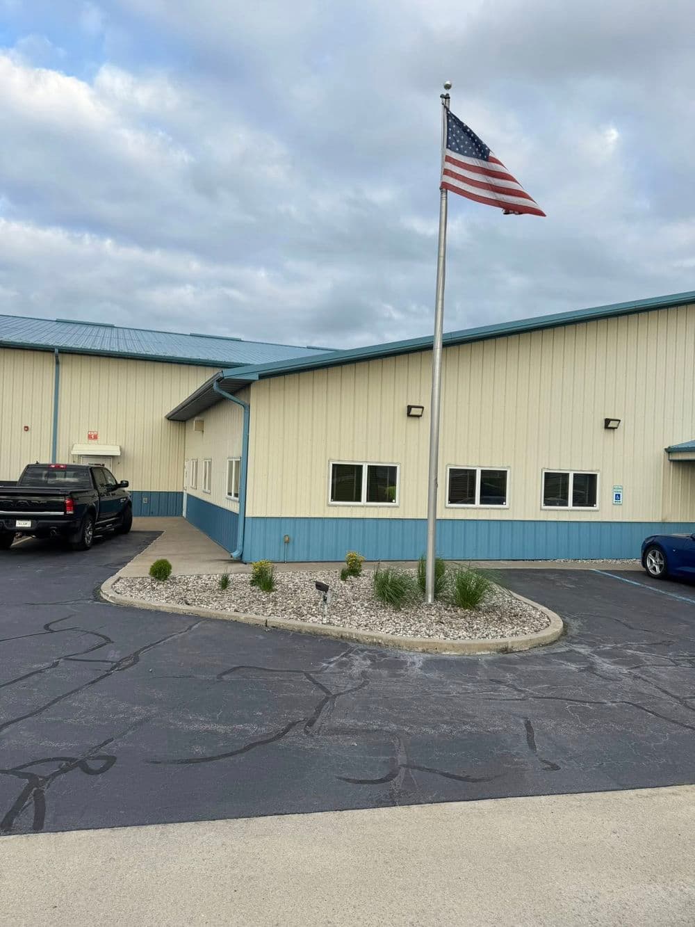 American flag flying outside a commercial building with a paved parking area and landscaping.