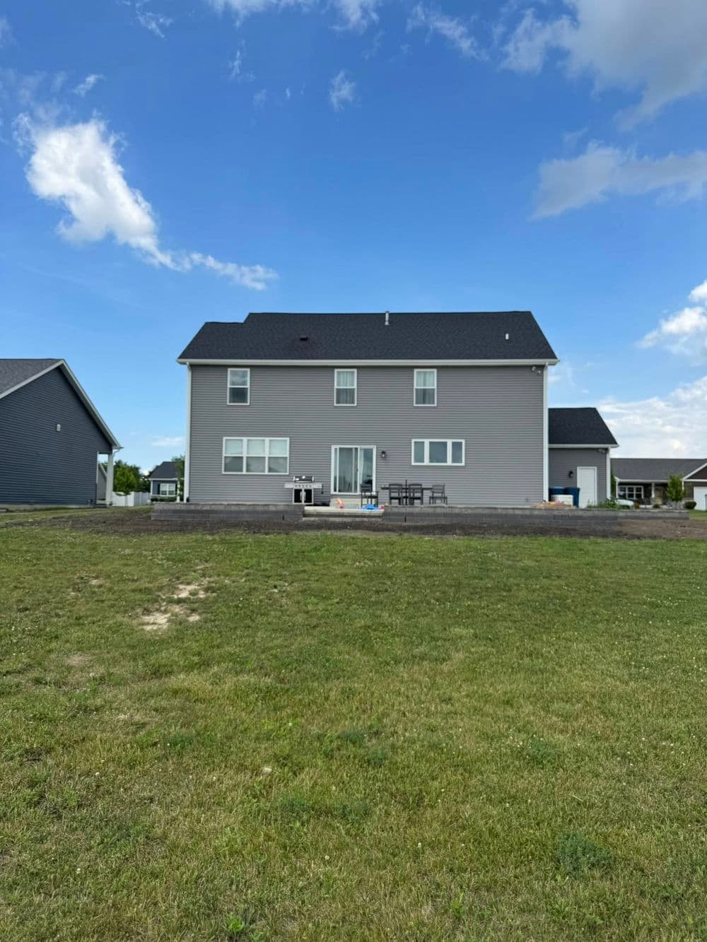 Two-story gray house with patio and lawn under a blue sky. Ideal for family living.