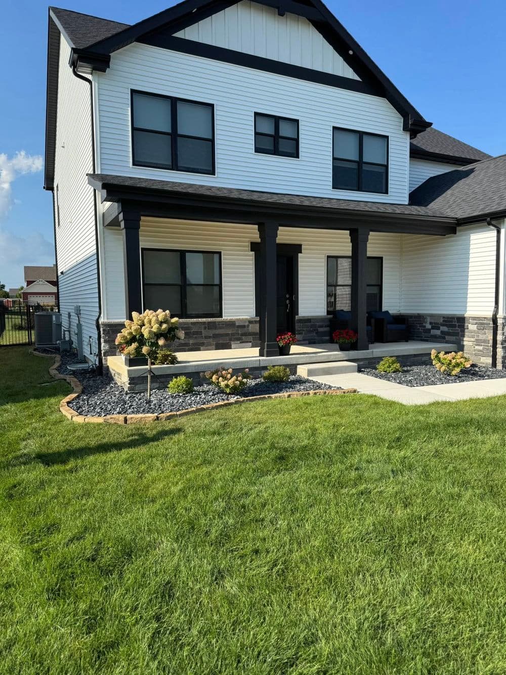 Modern two-story house with a front porch, landscaped yard, and flowering plants.