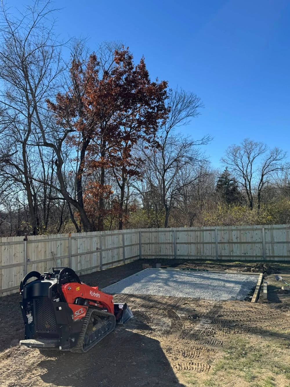 Kybota SCL track loader on a construction site with a fenced area and clear blue sky.