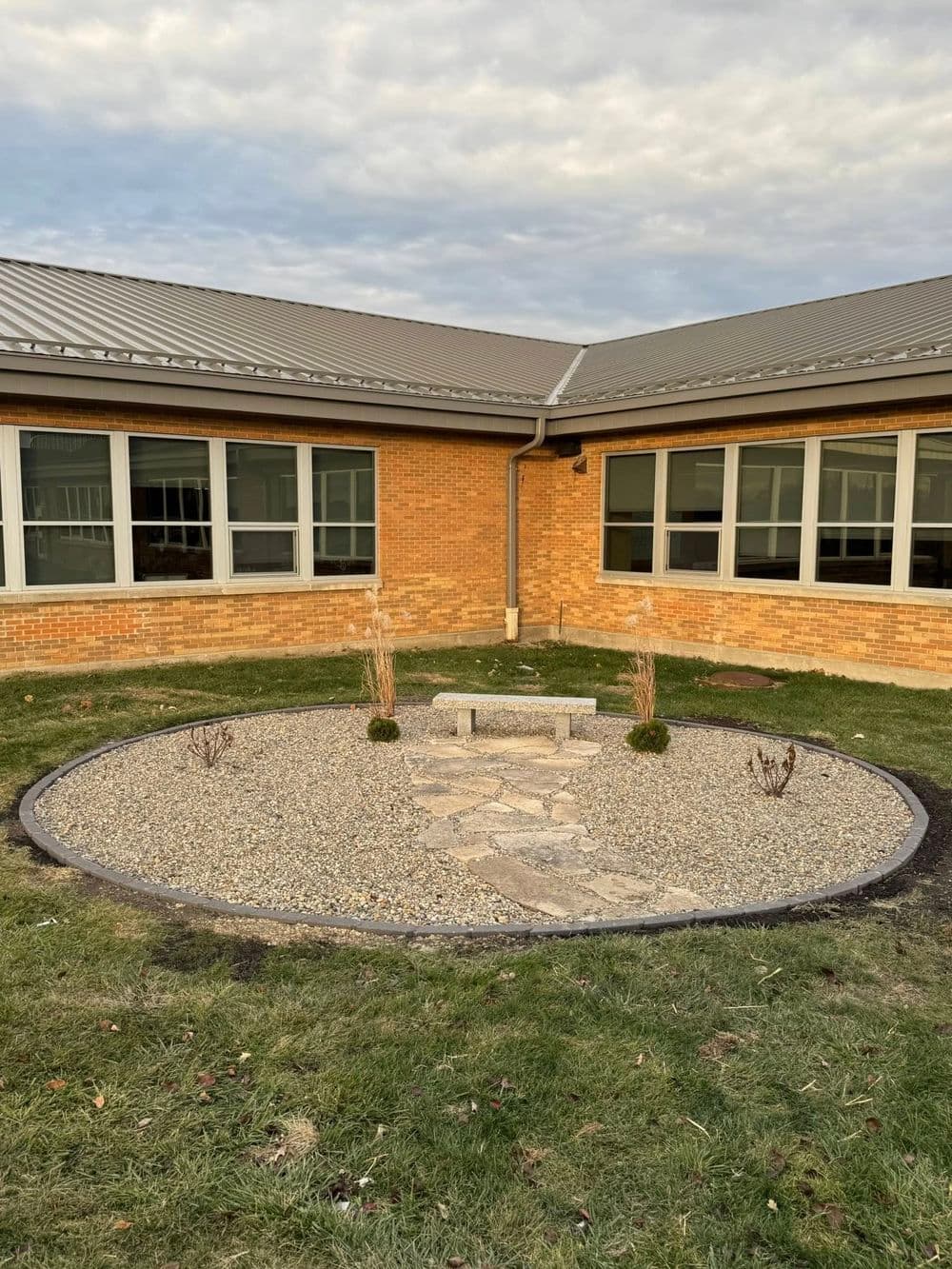 Outdoor seating area with a stone path surrounded by gravel and low shrubs near a school.